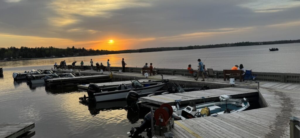 Fishing activity at Driftwood Lodge Dock on Lake Kabetogama, with boats lined up and people enjoying the calm water during sunset.