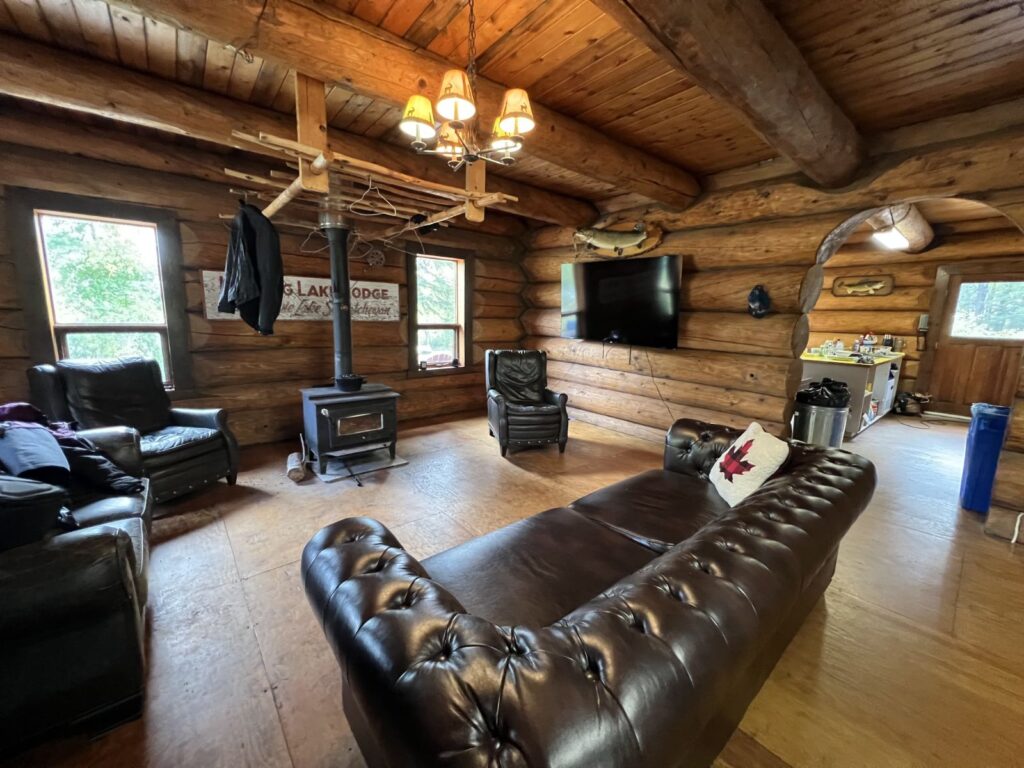 Log cabin living room with leather couches and a wood stove at the Kamuchawie Lake outpost